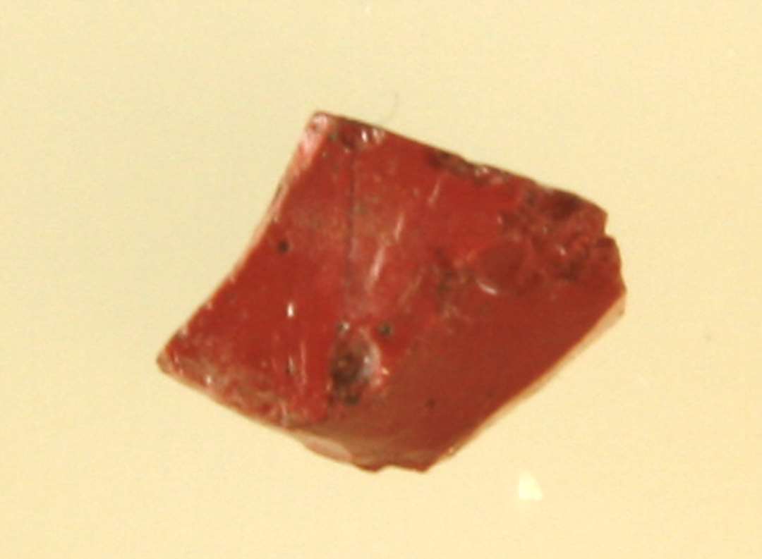 Fragment af mosaikstift af rødbrun, ugennemsigtig glasmasse.