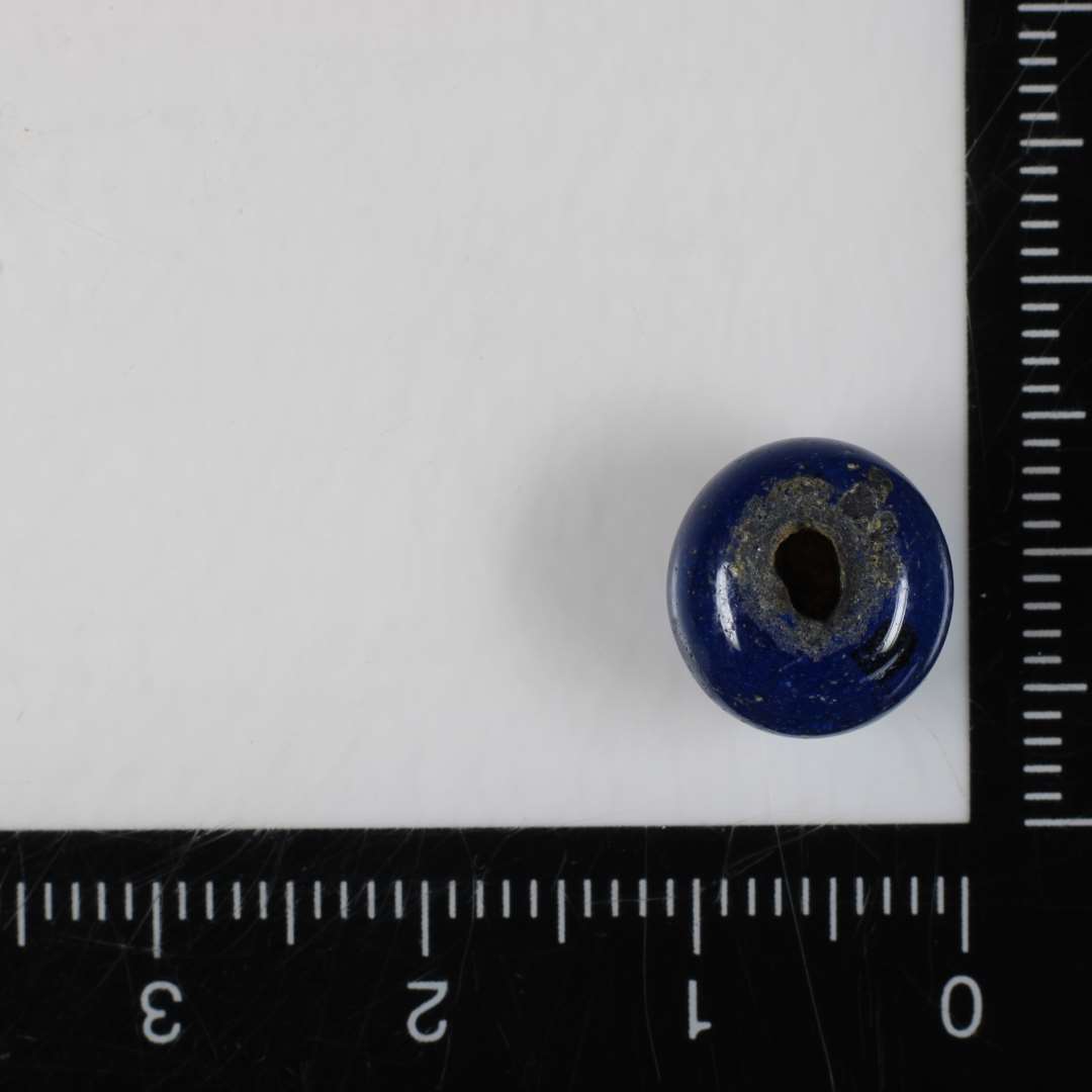 1 perle af afrundet ringform af blålig gennemsigtig glasmasse. 10 mm.