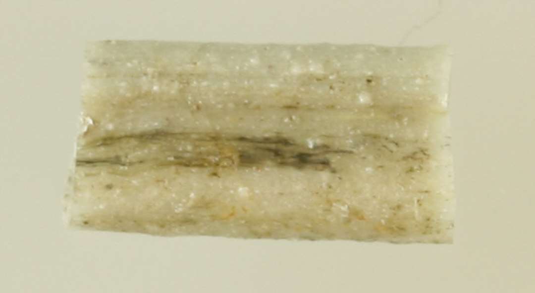 1 fragment af aflang, bændelformet glasstang af grålig ugennemsigtig glasmasse.
