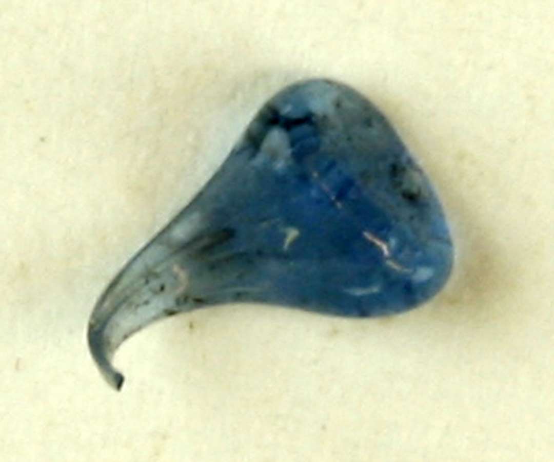 1 sammenklemt dråbe af smeltet, gennemsigtigt, blåligt glas udtrukket i en tynd ombøjet spids i den ene ende.