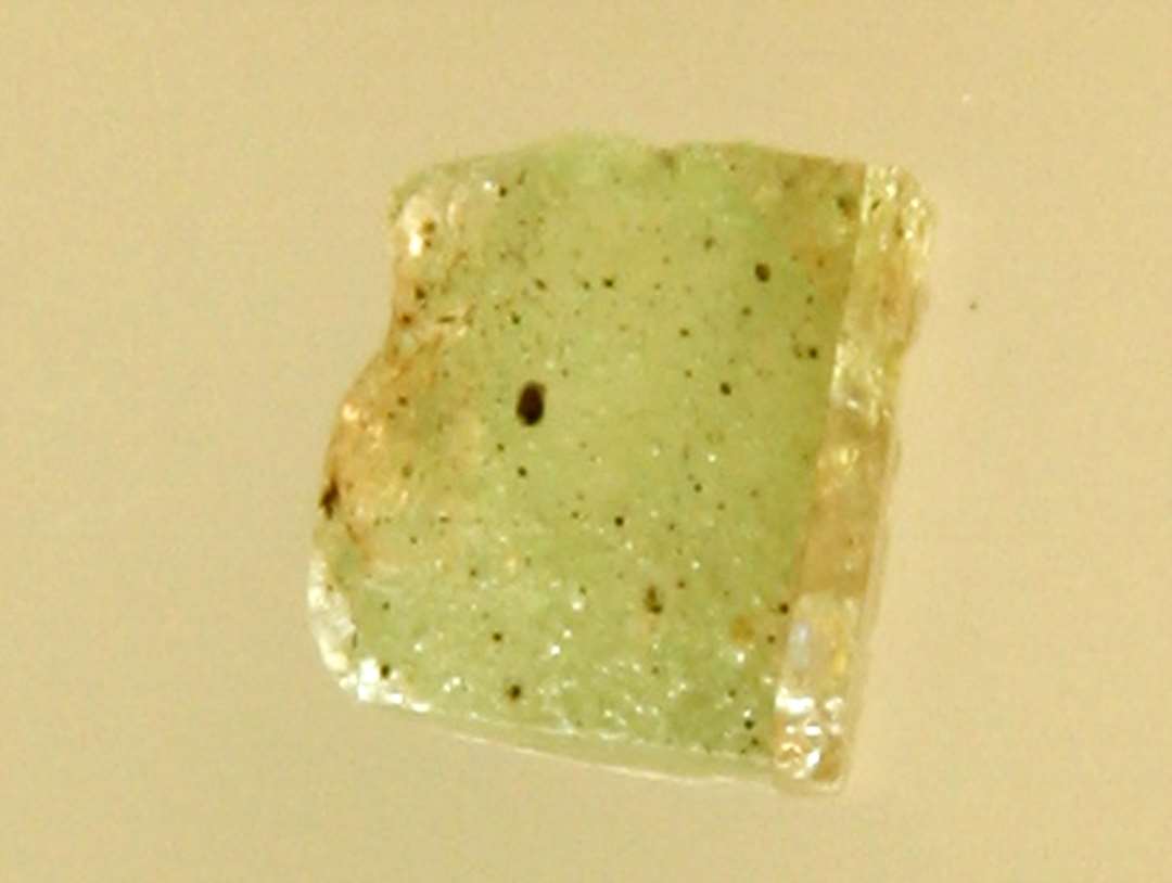 1 fragmenteret(?) mosaikstift af svagt grønlig gennemsigtig glasmasse med guldfoliebelægning på den ene side.