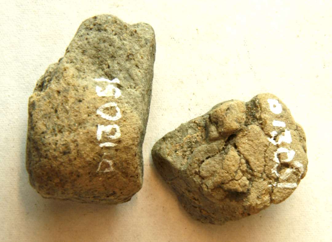 AMÆ 2 fragmenter af støbeform af gråbrændt ler, hvoraf det ene udviser spor af afglattet flade, der danner en art rammekant om et forsanket felt. Mål: 3,3 x 2,4 x 2,0 cm. og 2,5 x 2,1 x 1,7 cm.