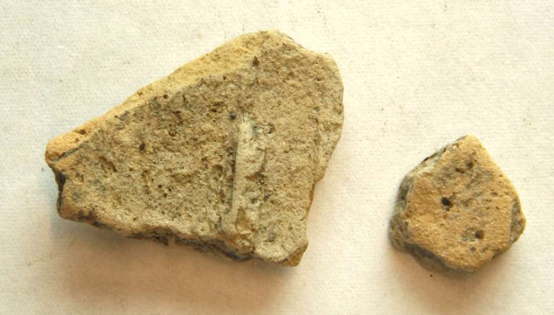 AMØ 2 fragmenter af støbeform af gråbrunligt brændt ler, antageligt et afspaltet yderlag af formen. Mål: 2,9 x 2,35 x 0,8 cm. og 1,3 x 1,20 x 1,2 cm. 