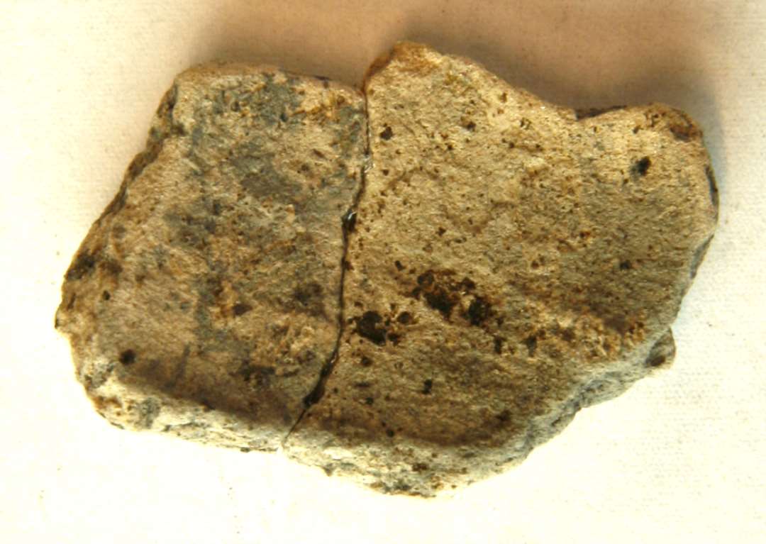 AMÅ 1 fragment (samlet af 2 stykker) af støbeform af gråbrunligt brændt ler, antagelig et afspaltet yderlag af formen. Mål: 4,0 x 3,0 x 0,85 cm. 