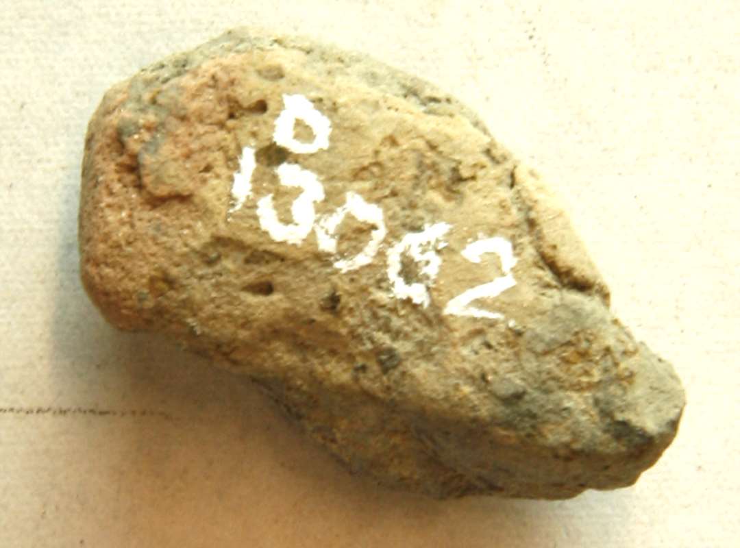 ANJ, 1 støbeformsfragment af gråbrunt, brændt ler med spor af en plan sideflade. Mål: 2,85 x 1,6 x 1,3 cm. 