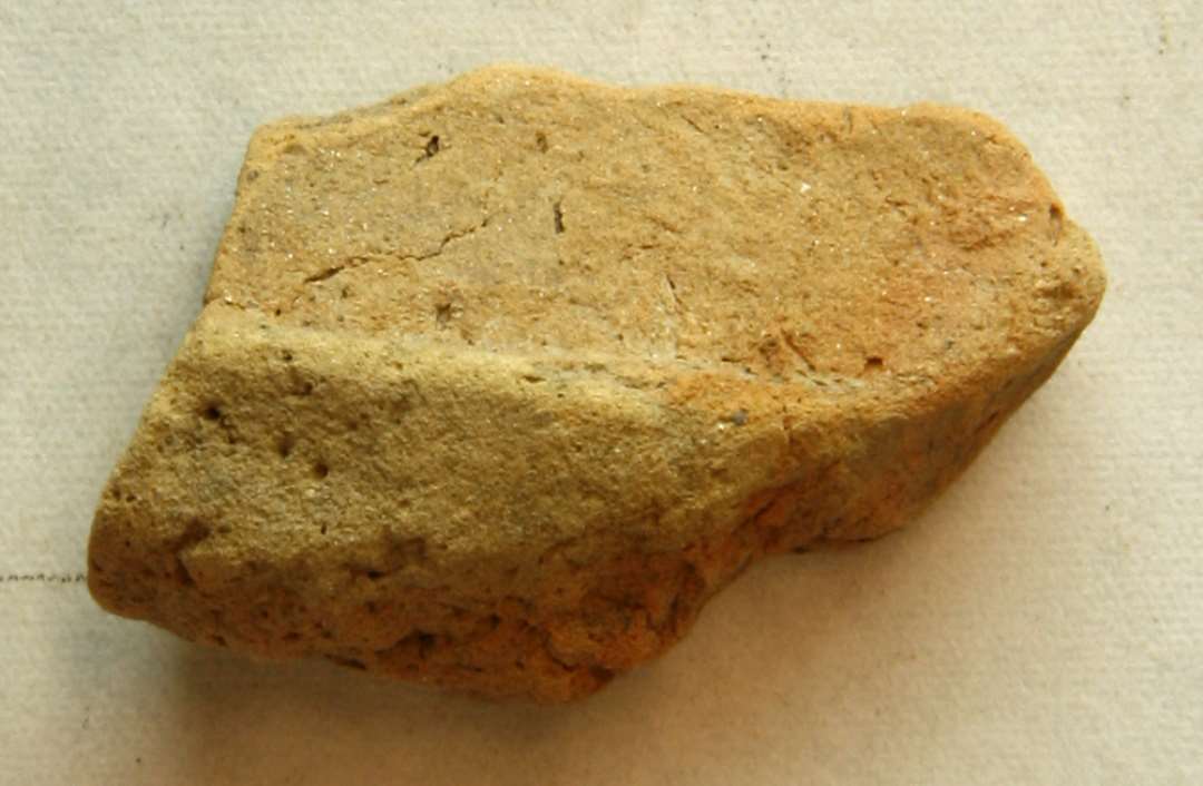 1 fragment af støbeformshalvdel af lysebrunt, fintmagret brændt ler med spor af forsænket, plan flade på indersiden. Mål: 2,7 x 2,0 cm. Tyk: 1,35 cm.