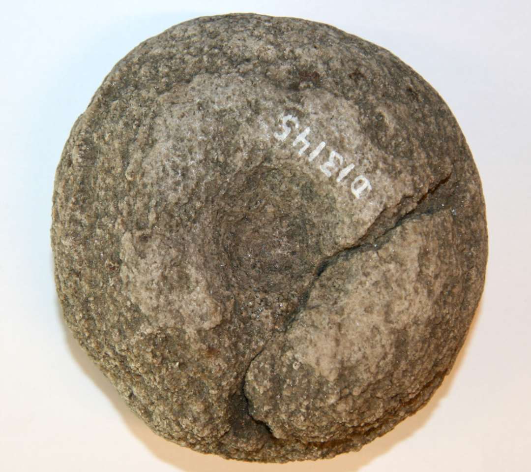 1 discosformet sten af ildskørnet bjergart. Den ene side er hvælvet, den anden er forsynet med en ret flad skålformet grube, ca. 0,9 cm dyb og ca. 3 cm. i diameter. Stenens diameter: 8,9 - 9,3 cm. Tyk: 4,0 cm.