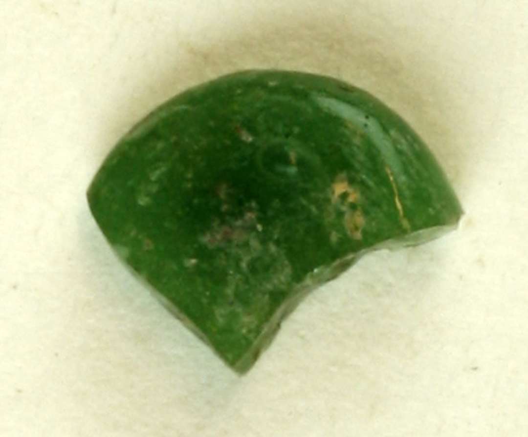 1 fragment af fladklemt, smeltet glasklump af delvis gennemsigtig, grønlig glasmasse.