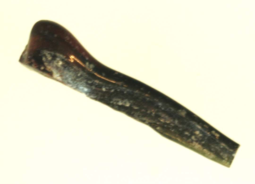 1 fladt udtrukket stykke glastråd med fortykkelse i den ene ende af sortrødbrunlig ugennemsigtig glasmasse.