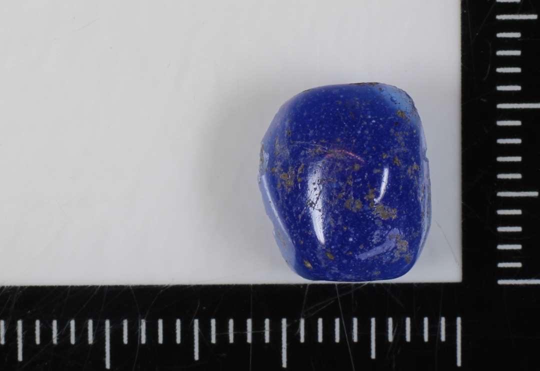½ perle, spaltet på langs, af cylindrisk form med facetteret overflade af blåligt, delvis gennemsigtigt glas. 10 mm.