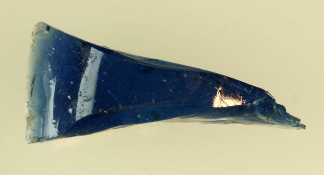 1 tykt stykke råglas af tresidet tilspidset form af gennemsigtig blålig glasmasse.