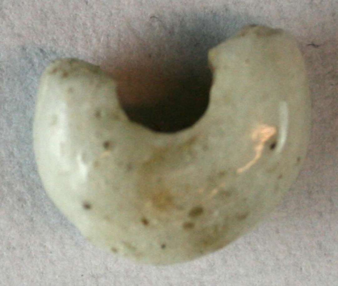 ½ perle af afrundet ringform af grålig, ugennemsigtig glasmasse spaltet på tværs. 11 mm.