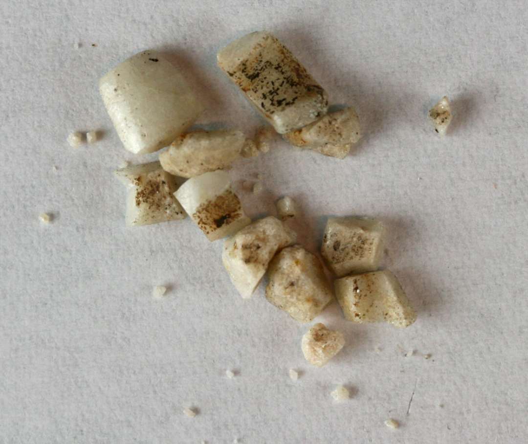 12 fragmenter fra knust, cylinderformet perle af hvidgrå, ugennemsigtig glasmasse.