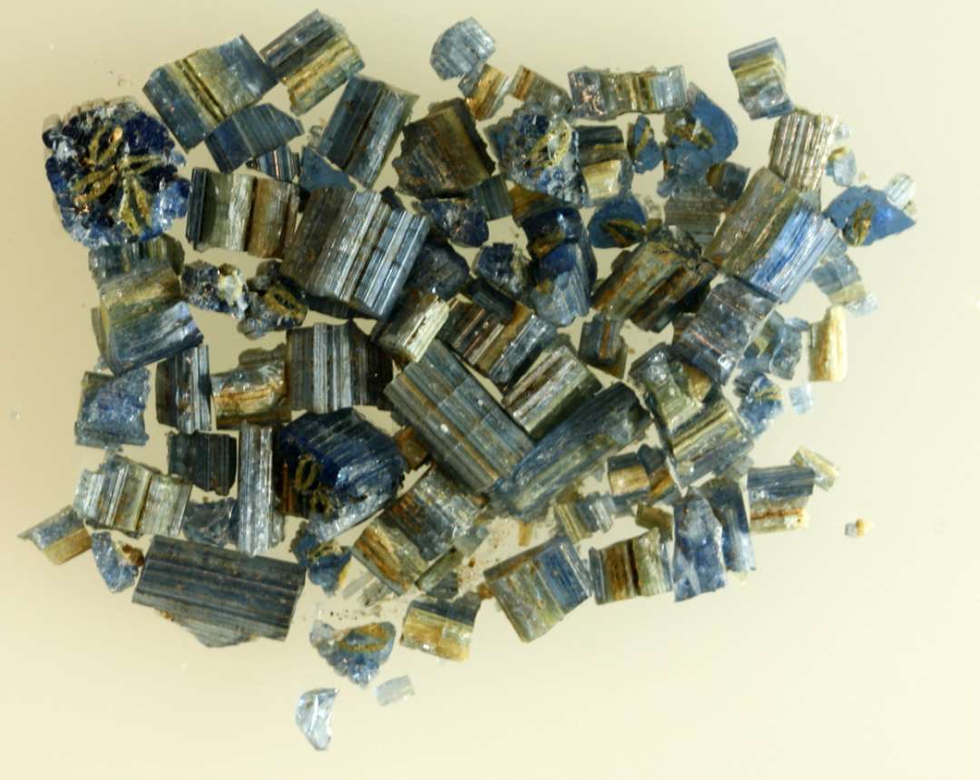 1 samling forknuste fragmenter fra glasstang (-stænger) af afrundet kvadratisk form dannet af sammensmeltede tråde af blåligt gennemsigtigt glas, hvori indgår et firebladet rosetmønster af tråde af gullig, ugennemsigtig glasmasse.