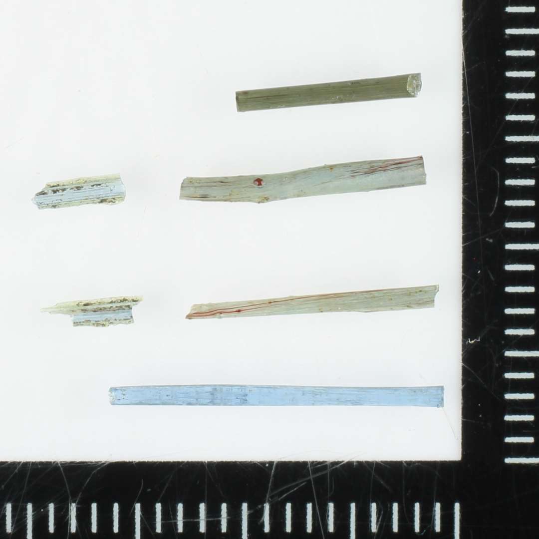 5 glastrådsfragmenter af stoppenålstykkelse af gennemsigtig grålig til svagt blålig glasmasse. I enkelte af de grå tråde indgår hårfine årer af rådbrunlig ugennemsigtig glasmasse.