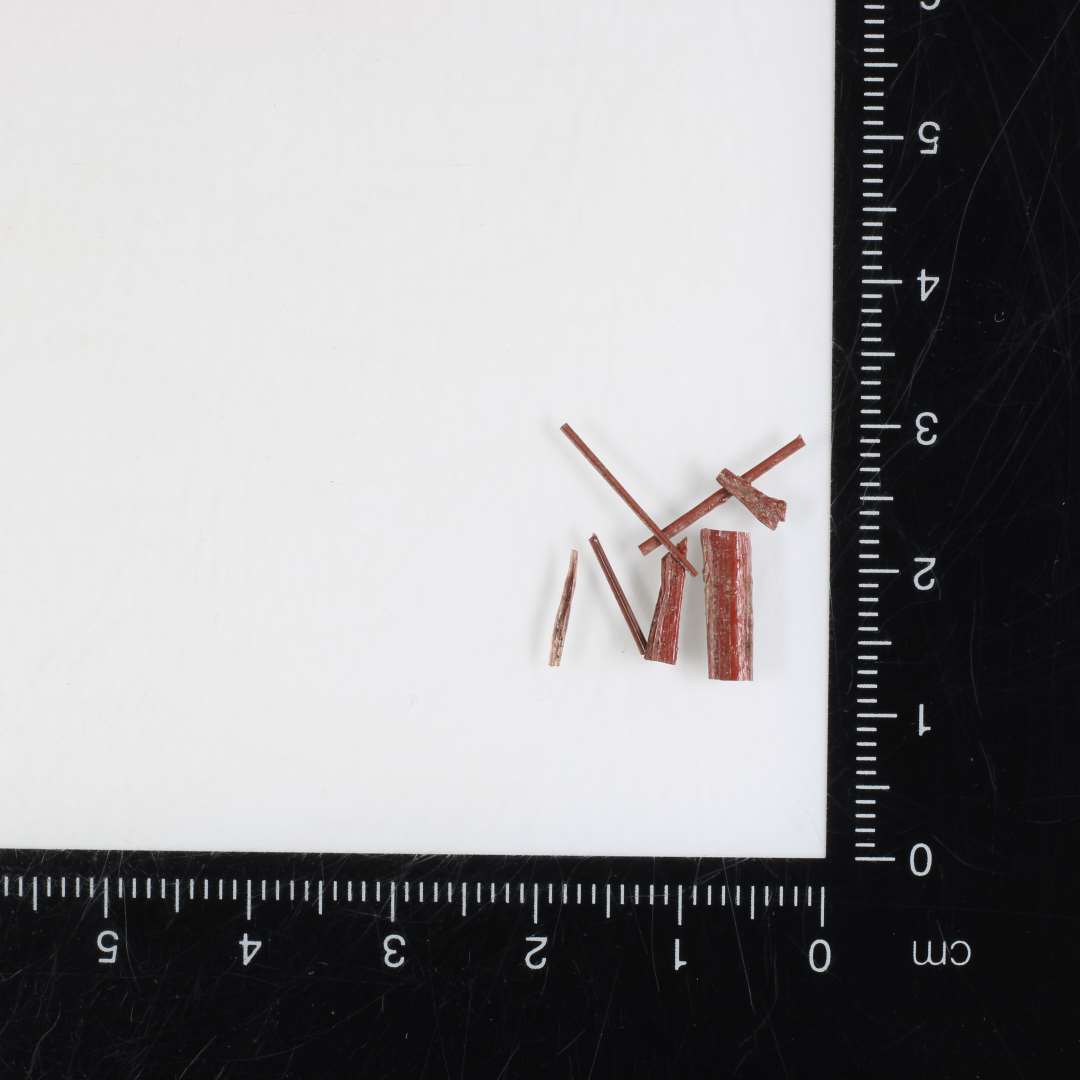 6 fragmenter af glastråde af rødbrunlig ugennemsigtig glasmasse, de tre af flad bændelagtig form, de øvrige nåleformede, det ene 3,6 cm. langt.