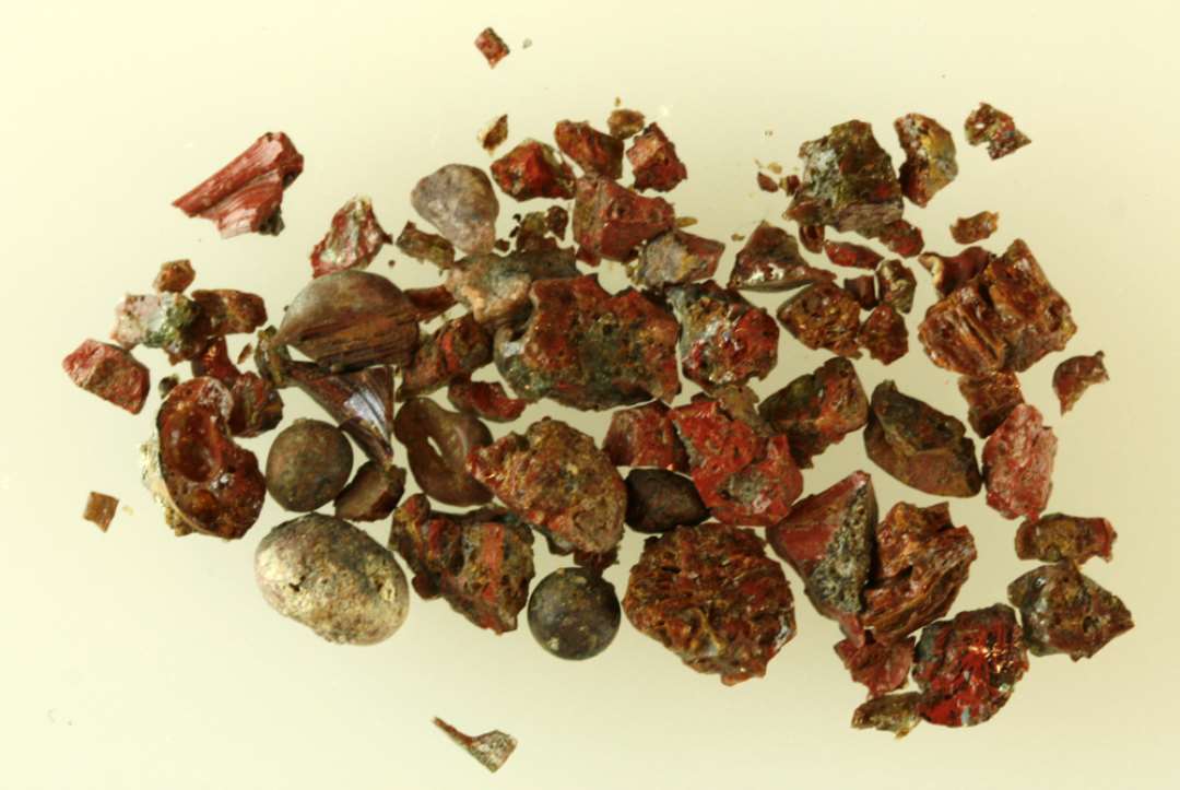 En samling af forknuste, smeltede og sintrede stumper af rødbrunlig ugennemsigtig glasmasse.