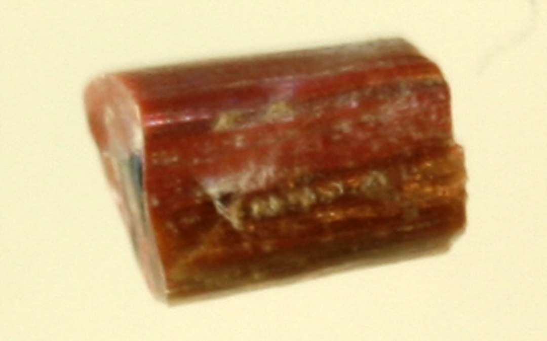 1 fragment af glasstang af afrundet kvadratisk tværsnitsform af rødbrunlig ugennemsigtig glasmasse med en forgrenet midteråre af mørkt, ugennemsigtigt glas.