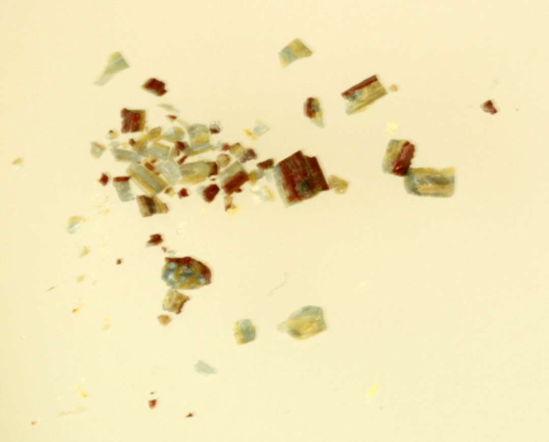 En samling forknuste fragmentstumper fra glasstang bestående af gennemsigtig blålig og ugennemsigtig gullig glasmasse omgivet af et yderlag af rødbrunlig ugennemsigtig glasmasse.