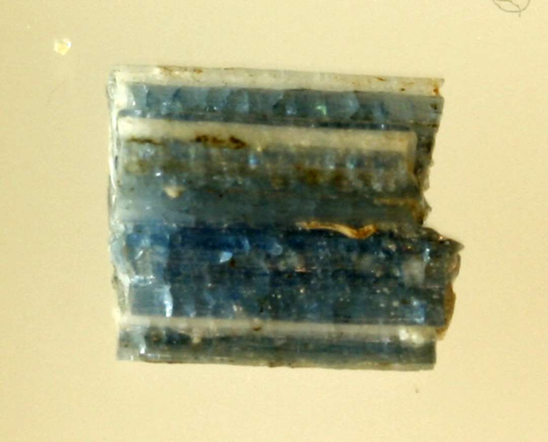 1 fragment af glasstang dannet af sammensmeltede tråde af blåligt gennemsigtigt glas, hvori indgår tråde af hvid ugennemsigtig glasmasse, der i tværsnit danner et korsformet mønster.