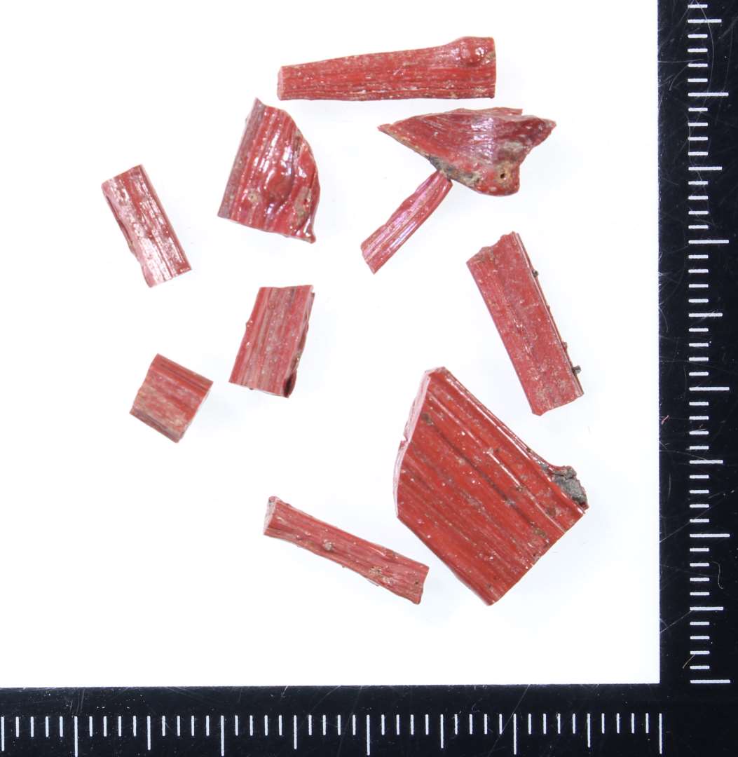 10 fragmentstumper af varierende smallere og bredere stangform af rødbrunlig ugennemsigtig glasmasse.