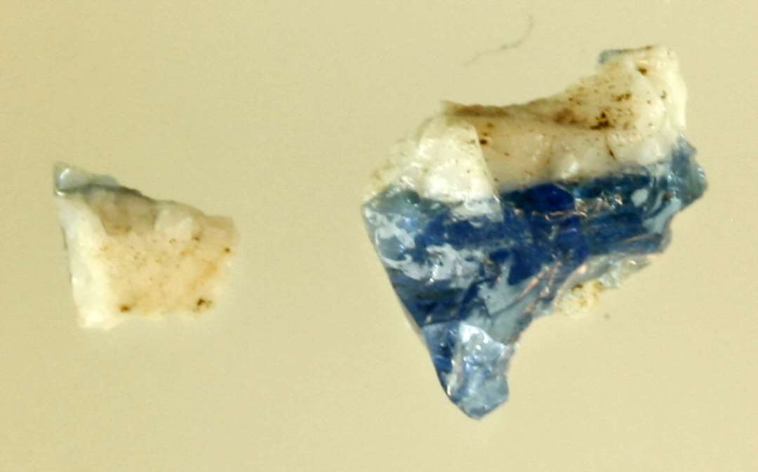 2 forknuste glasstumper af sammensmeltet ugennemsigtig hvidgrå og gennemsigtig blålig glasmasse.
