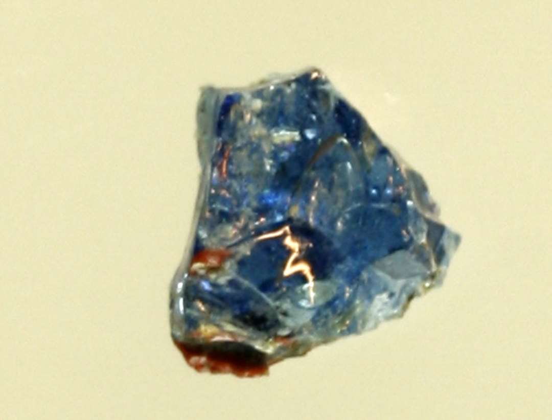 1 ubetydelig fragmentstump af smeltet, gennemsigtigt, blåligt glas med parti af rødbrunlig, ugennemsigtig glasmasse.