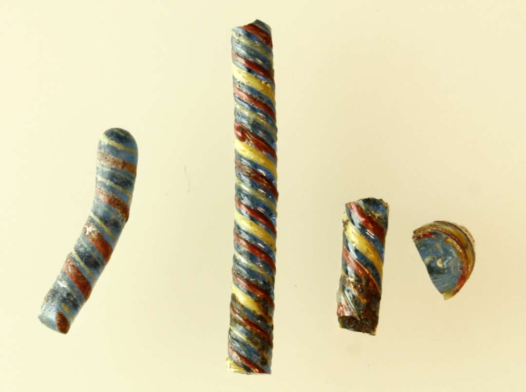 4 fragmenter af tovsnoede glasstænger, det ene smeltet og let bøjet, af blåligt, gennemsigtigt glas omviklet med tynde tråde af ugennemsigtig gul og rødbrunlig glasmasse i S-snoet forløb.