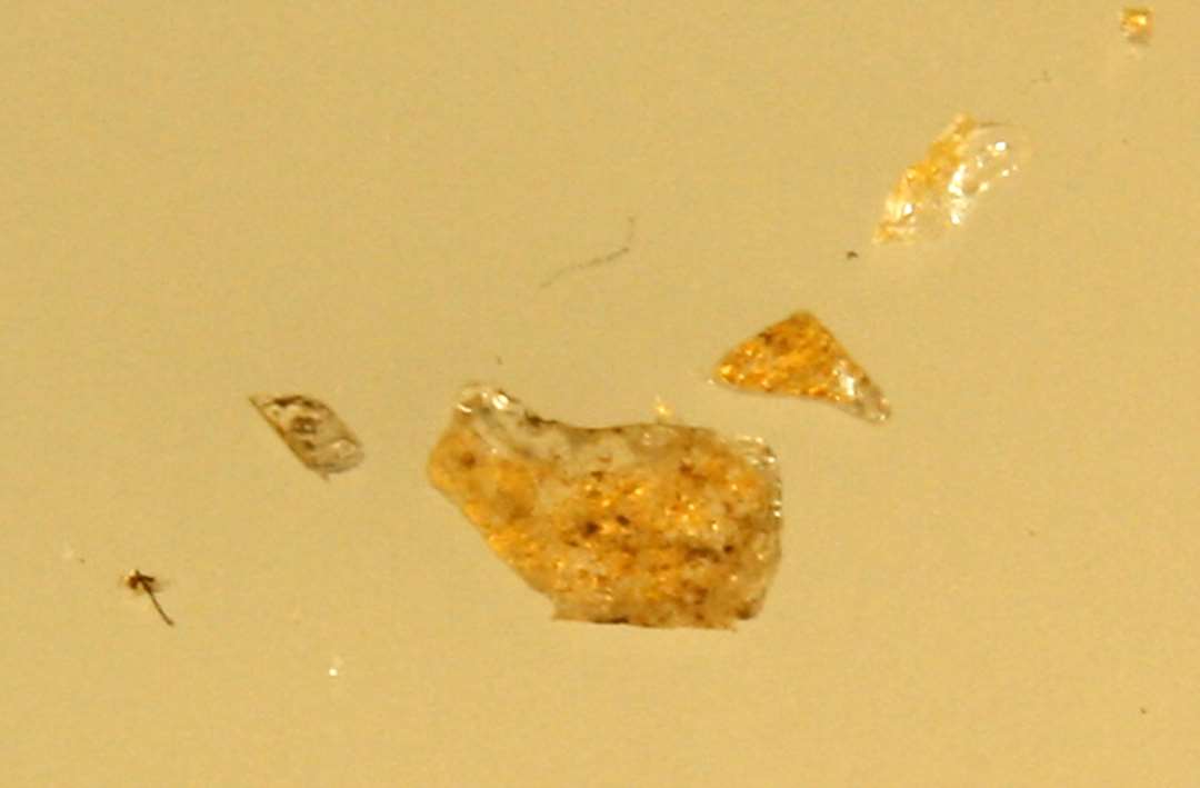 1 knapt millimetertykt fragment af klar glasskive med guldfoliebelægning på den ene sideflade hidrørende fra oversiden af glasmosaikstift.
