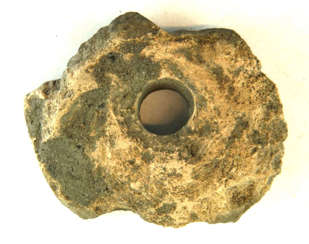 1 stærkt fragmenteret midterparti af discosdormet vævevægt af gråbrunlig brændt lermasse. Mål: 8,5 cm.