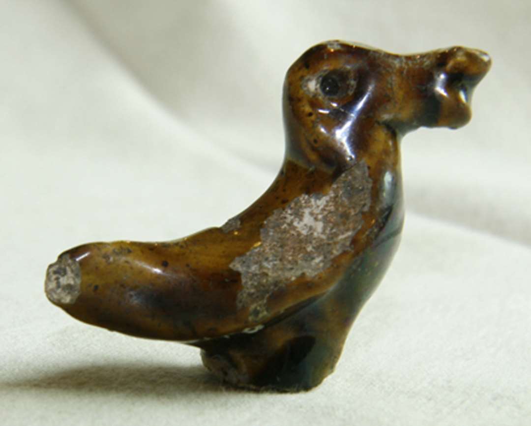 Figur af glaseret pibeler, forestillende en and. Fra neden et hul op i figuren, til pind eller lignende. 5x3,5 cm. Marionet. Legetøj.