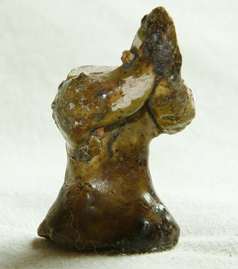 Figur af glaseret pibeler forestillende en person med hænderne samlet i bøn. Hovedet mangler. h: 4,5 cm.