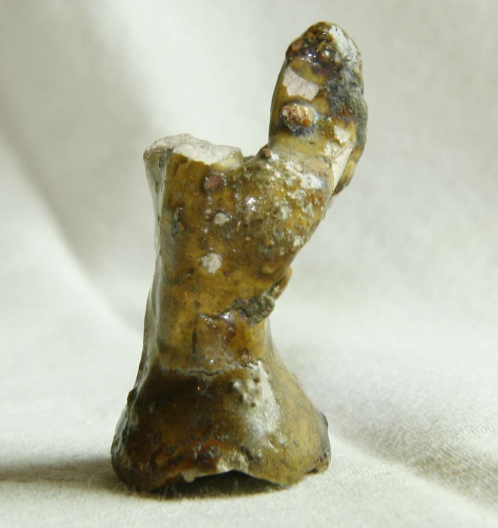 Figur af glaseret pibeler forestillende en person med hænderne samlet i bøn. Hovedet mangler. h: 4,5 cm.