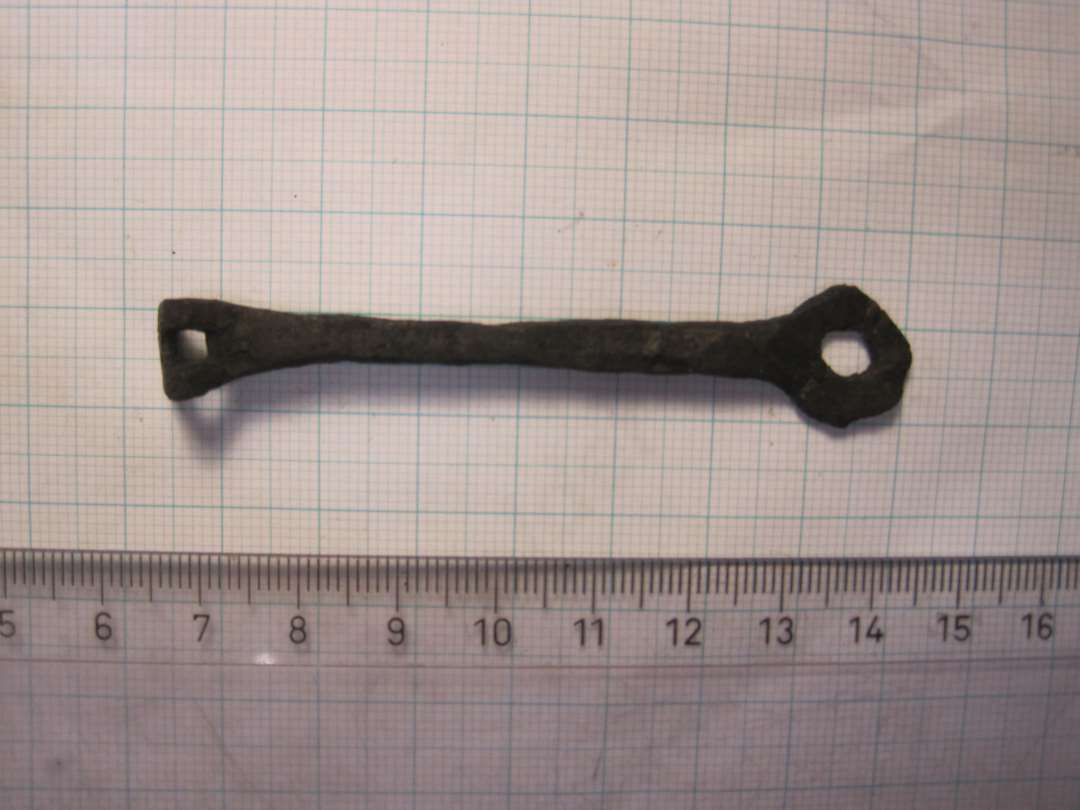 En nøgle med cirkulært hoved, dens kam er ombøjet i en næsten ret vinkel på skaftet. Længde: ca. 7,5 cm.