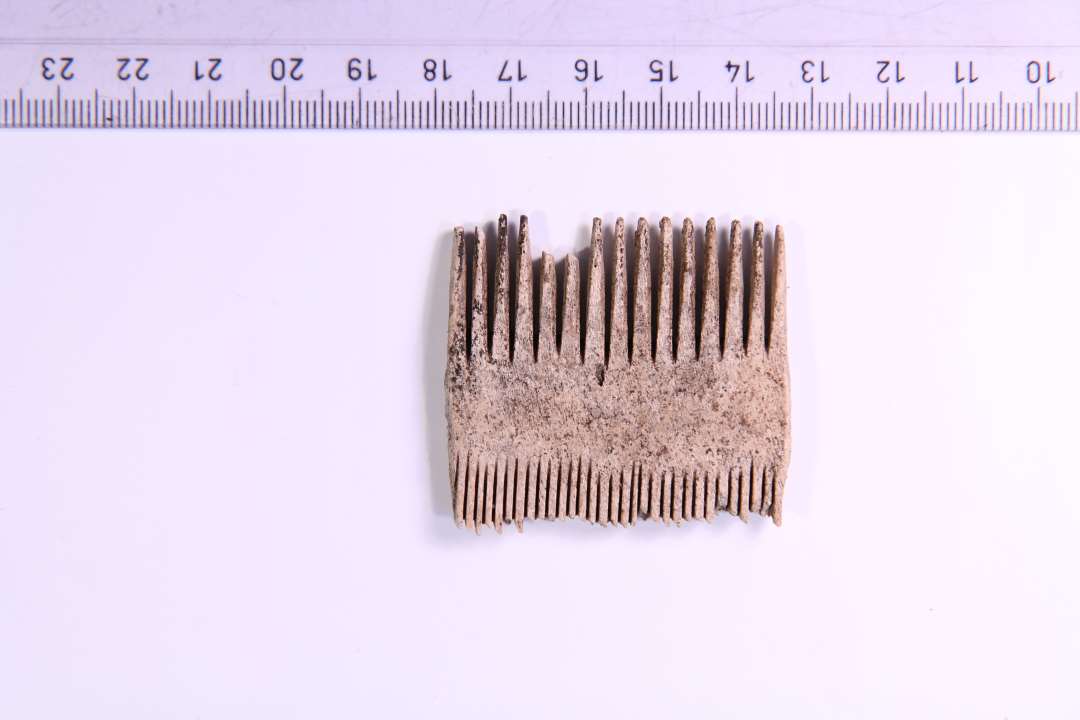 Dele af dobbeltkam af ben i et stykke med både store og små tænder. Højde: 4 cm. Bredde: 4,5 cm. Uden udsmykning.