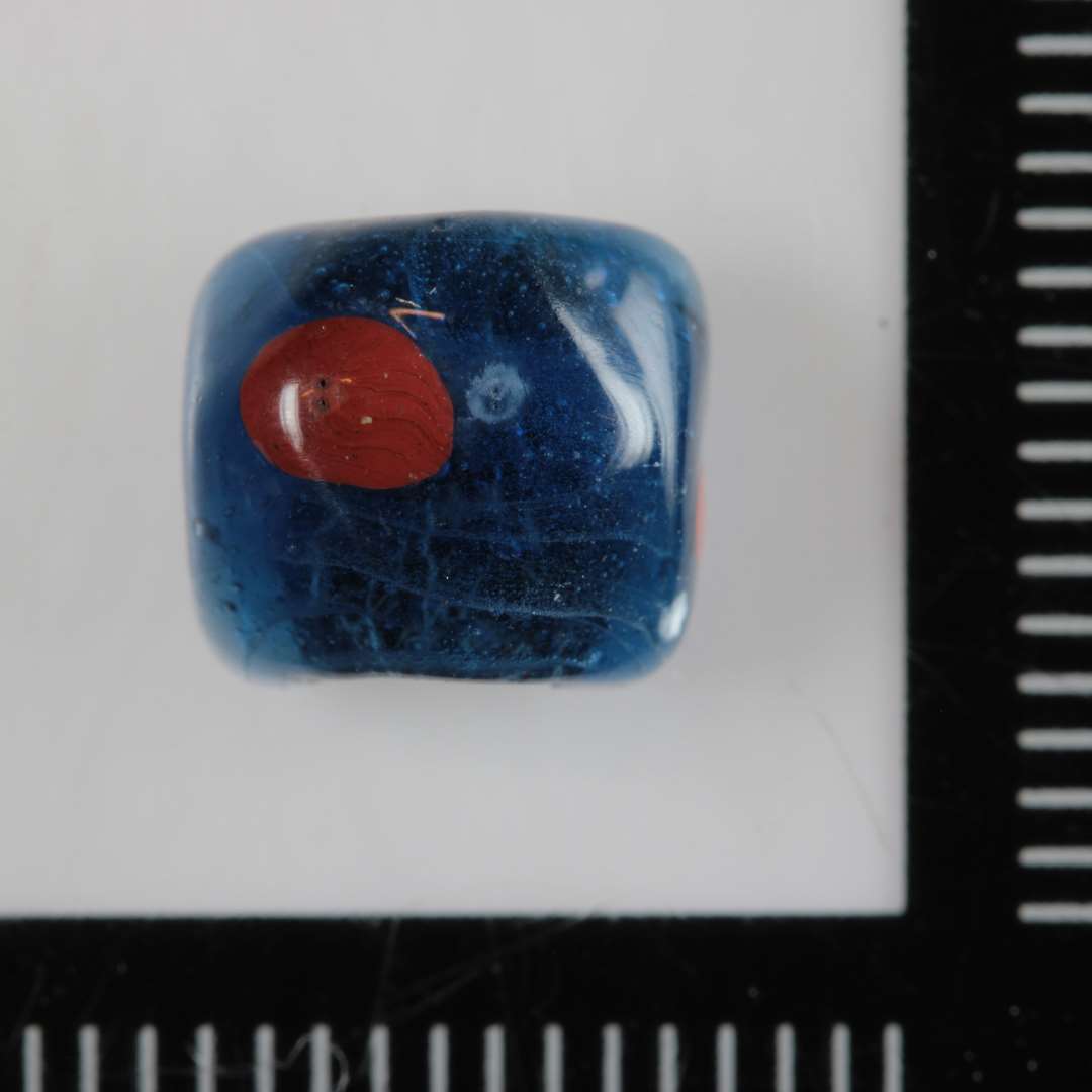 ½ perle af klart blåligt glas med facetteret sidekant, hvori med mellemrum er indsmeltet klatter af rødbrunligt glas.