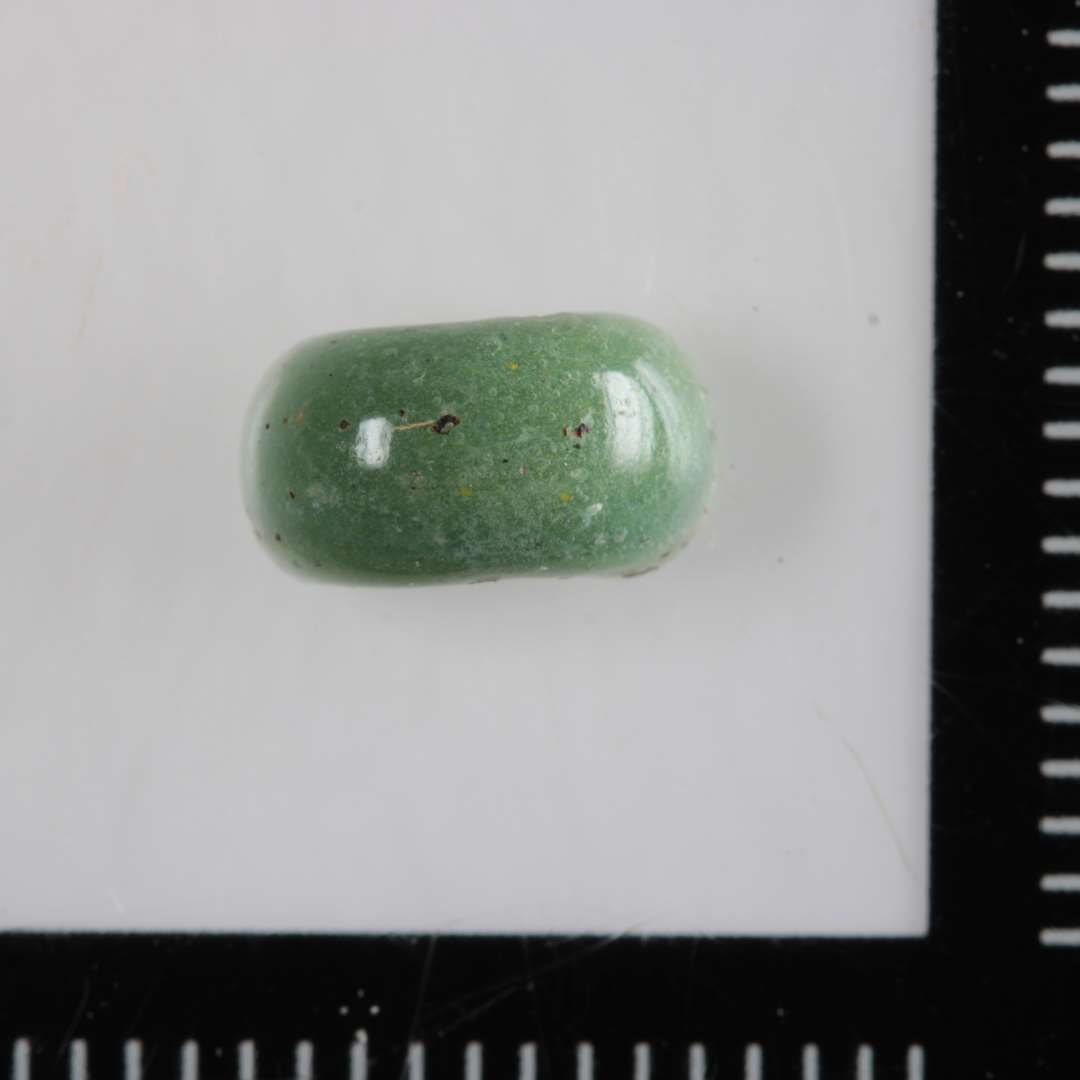 1 fragment af glasperle af afrundet skiveagtig form og af ugennemsigtig lys grønlig glasmasse.