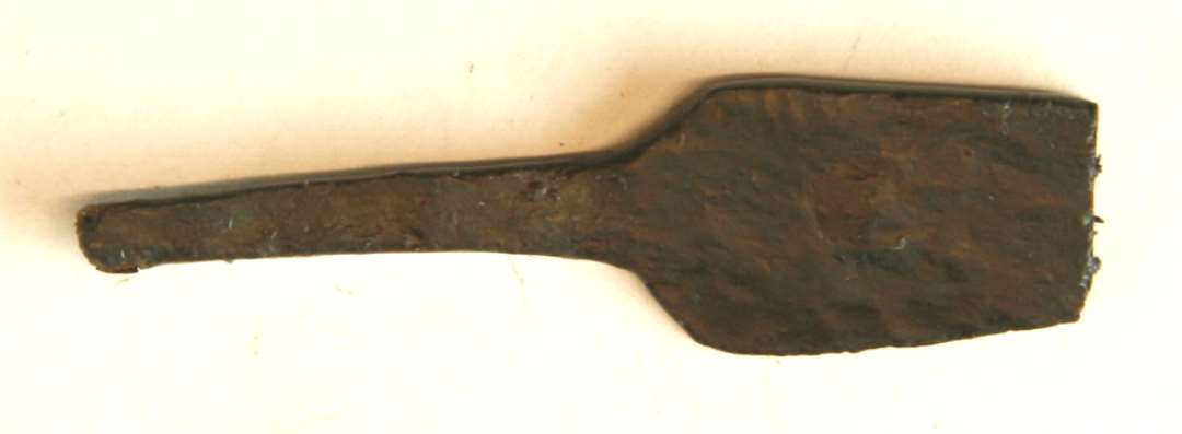 1 knivsblad af jern med smal forsænket skafttunge. Bladryggen danner et stumpvinklet knæk tæt ved spidsen. L : 6,3 cm.