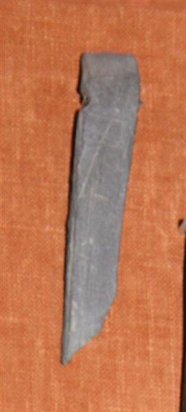 1 fragment af flad, tynd, opslidt hvæssesten af grålilla skifer. Nær den ene ende har stenen haft et ophængshul, men er spaltet på langs midt igennem dette. L : 7,4 cm. Br : 1,4 cm. St. tyk : 0,85 cm.