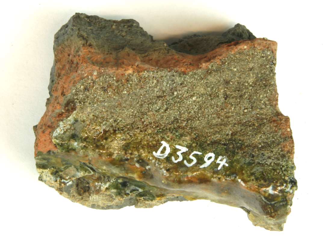 1 fragment af rødgrålig sintret tagsten ( ? ) med ujævn grønlig blyglasur på den ene sidekant.