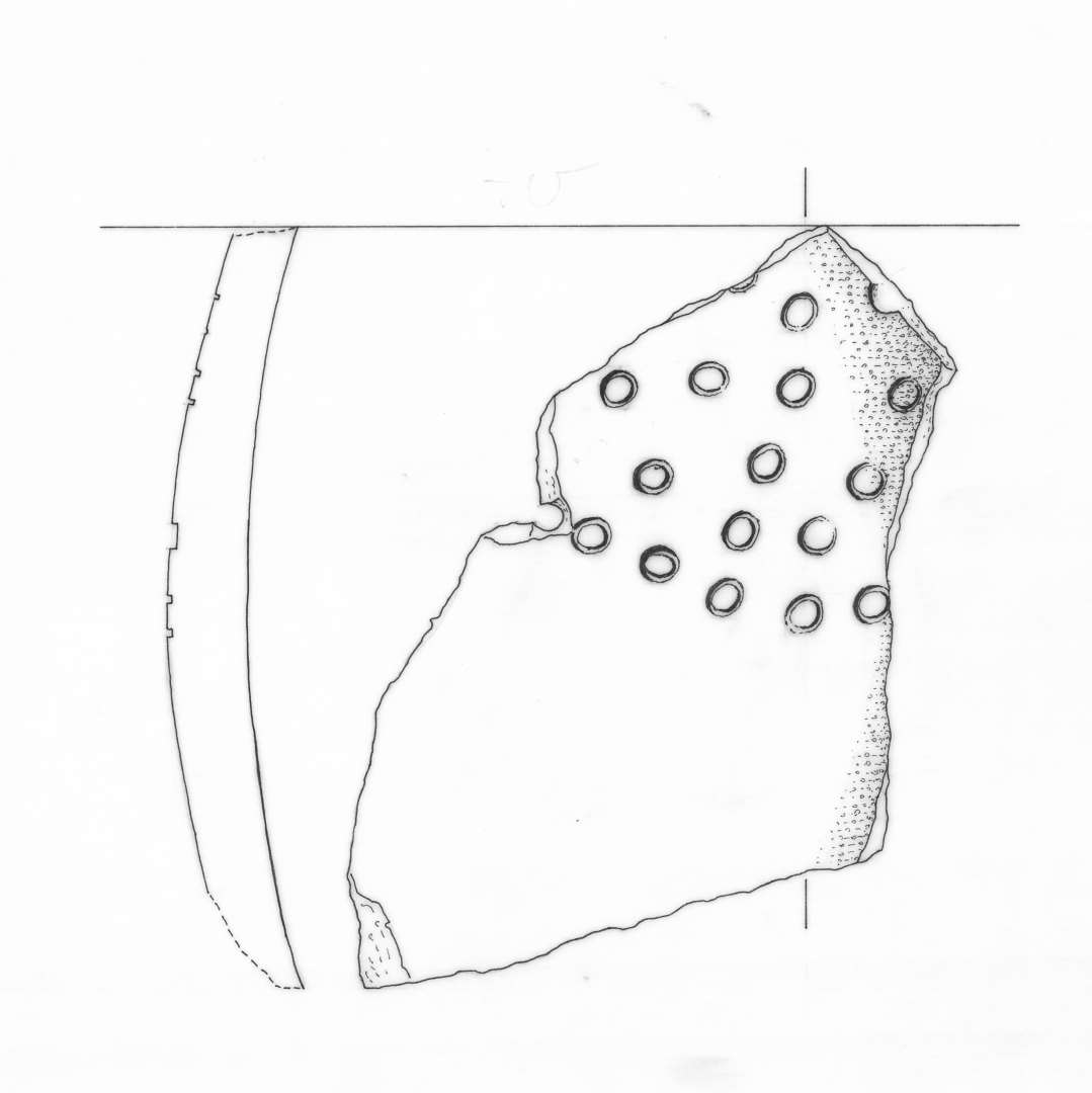 1 sideskår af gråbrunligt, magret lergods med indstemplet cirkelornamentik. Et klinkehul ses i randkanten, gruppe 5.