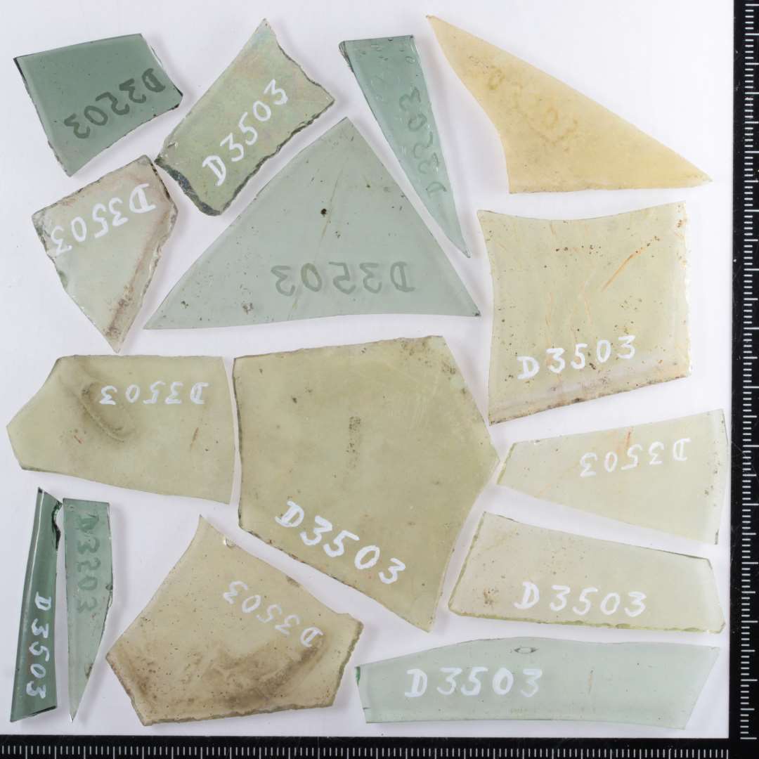 15 fragmenter af ruder af gennemsigtigt, grønligt glas, flere med spor af afnapning i kanten. Største mål: 2,5-6 cm.