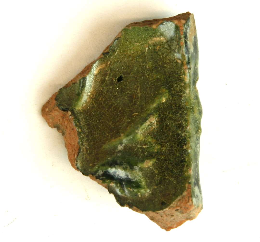 1 fragment af rødbrændt lergods med grøn glasur, gruppe 1. Største mål: 5 cm.