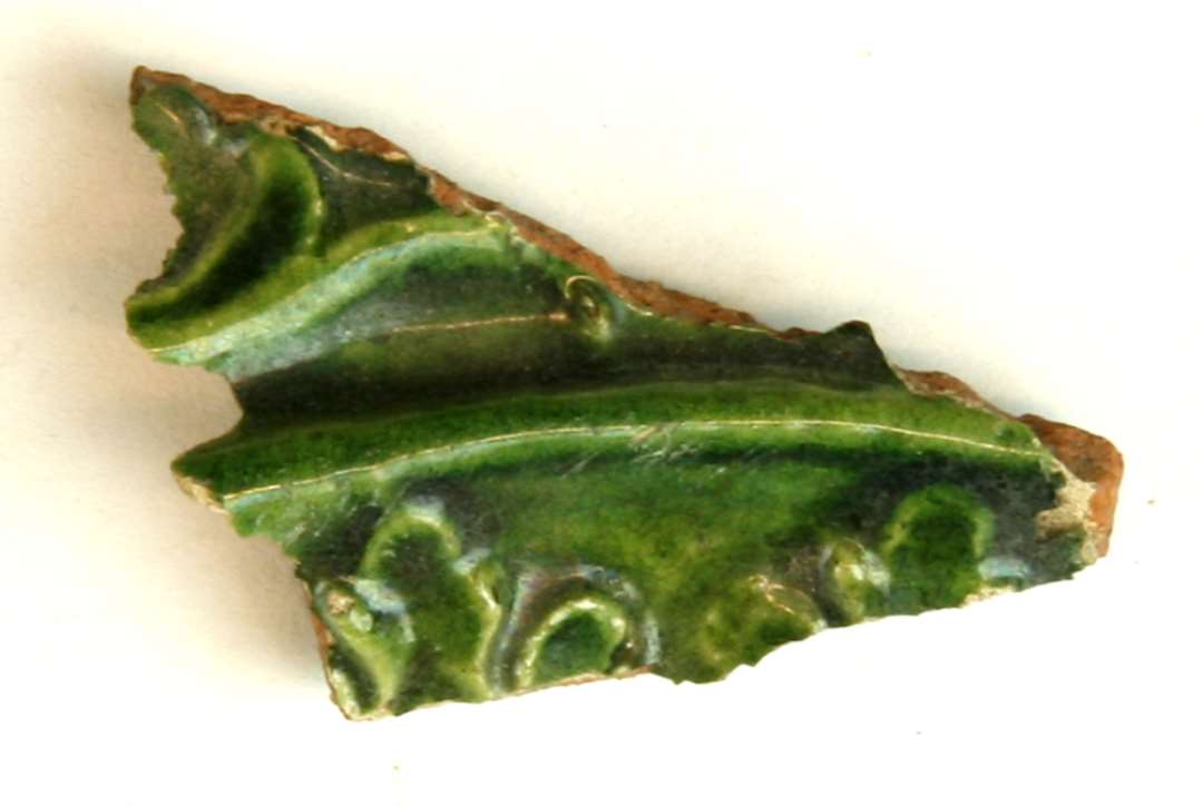 1 fragment af ornamenteret, grønglaseret kakkel. Største mål: 4,5 cm.