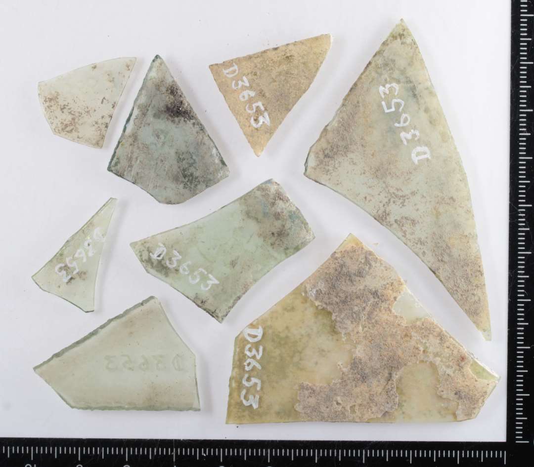 9 mindre fragmenter af rudeglas af iriseret, klart, let grønligt glas, flere med spor af afnapning i kanterne. Største mål: 2,5-7,5 cm.