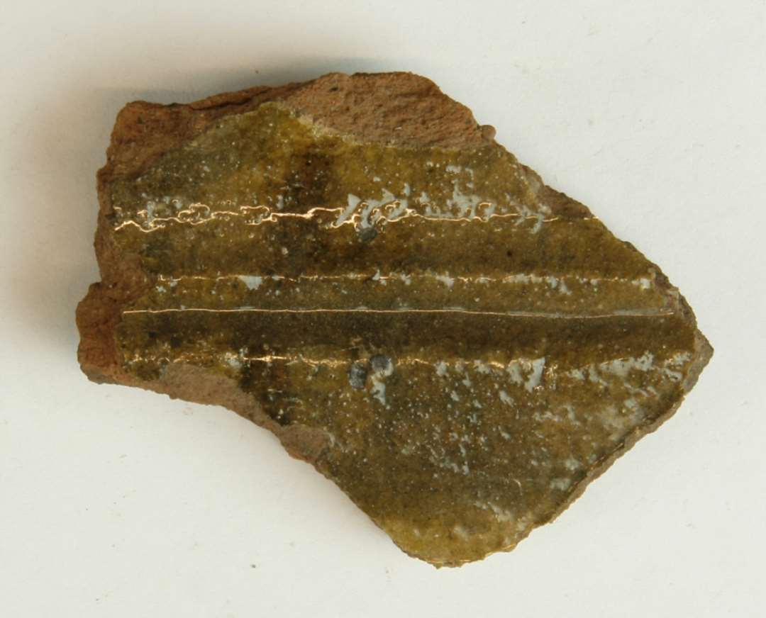 1 fragment af kakkelramme af rødbrændt lergods, hvorover klar blyglasur. Størstemål: 6,5 cm.