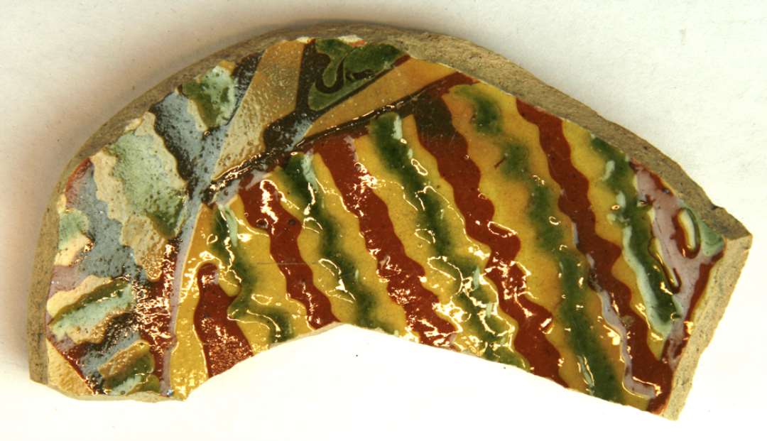 1 bundskår fra fad af gulligt, blyglaseret lergods med dekoration i forskellige toner af rødlersbegitning og grøn farve på indersiden, gruppe 1.