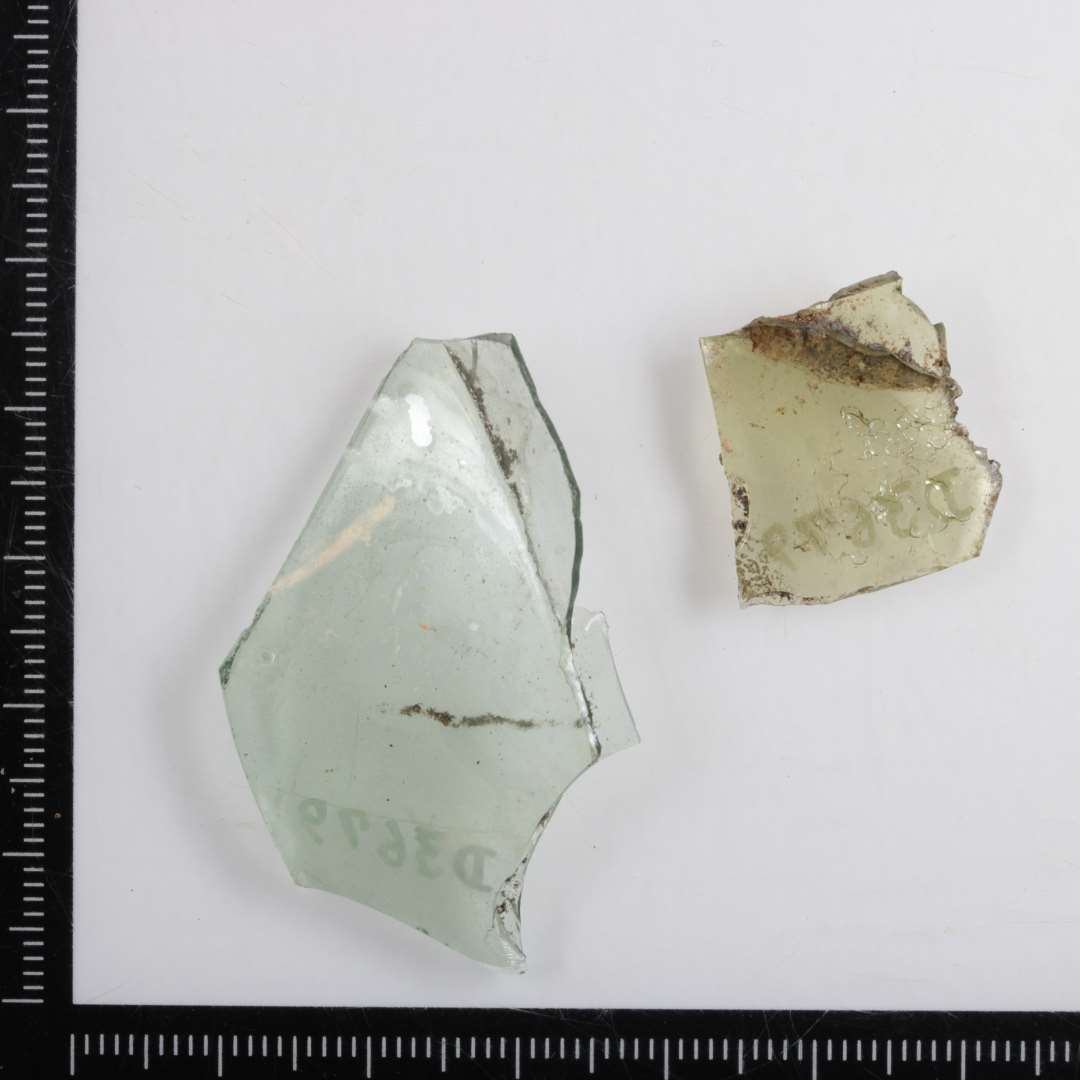 2 fragment af det øverste af en fod af klart, let grønligt, glas fra stangenglas.