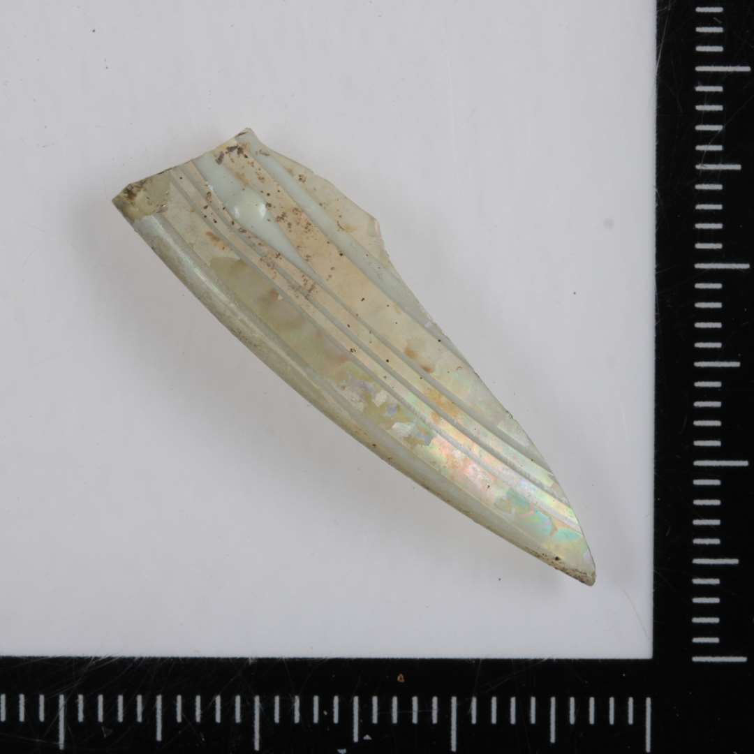 1 fragment af fodrand eller mundingsrand af iriseret, klart glas med indlagte og pålagte streger af hvidt glasmasse.