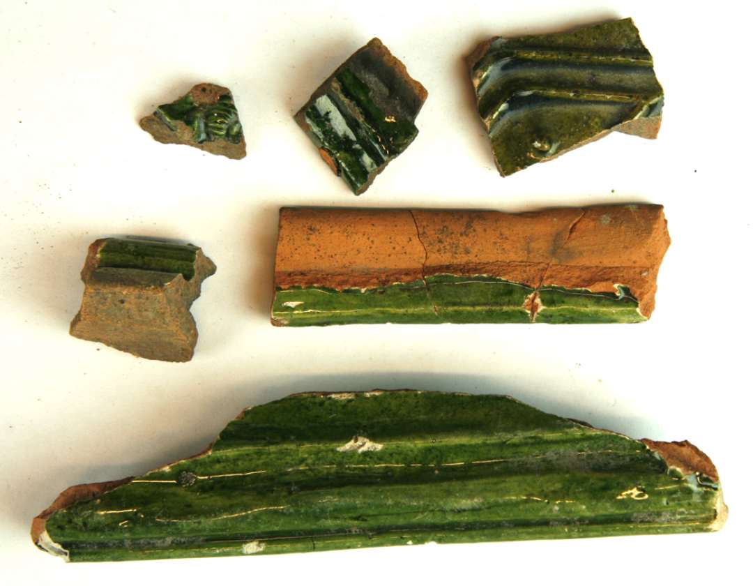 6 fragmenter af grønglaserede kakler, heraf 4 rammestykker og 2 midterfletsstykker. Største mål:  3-17 cm.